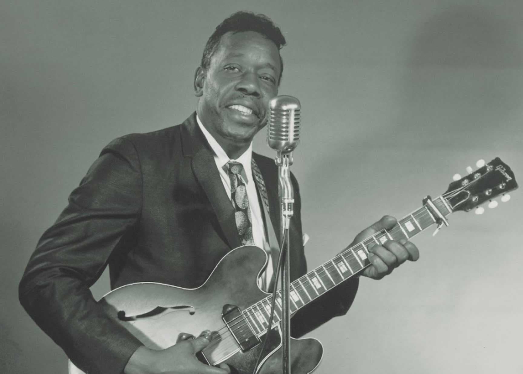 Slim Harpo holding guitar beside a vintage microphone