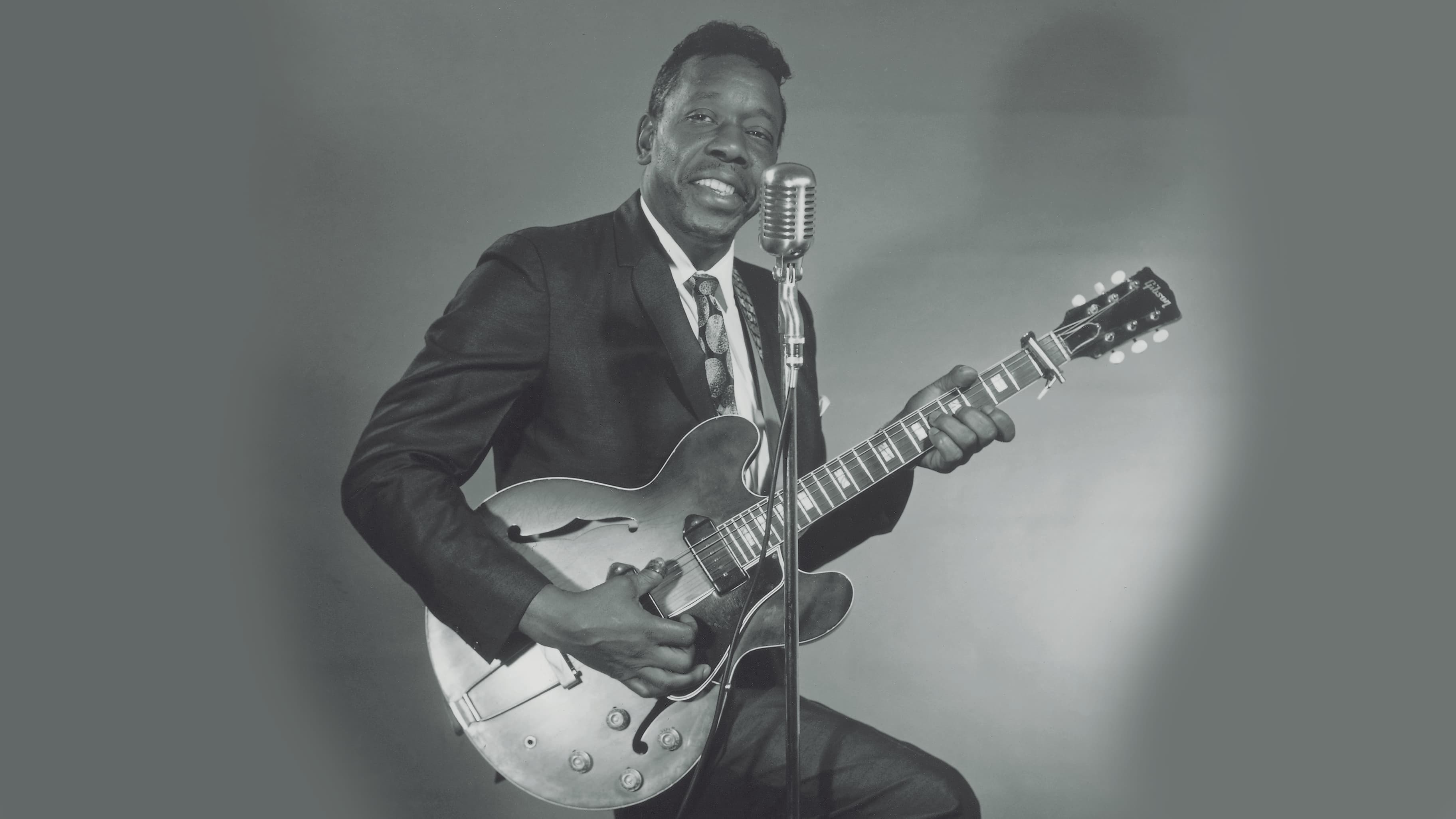 Slim Harpo holding guitar beside a vintage microphone in a wide archival photograph